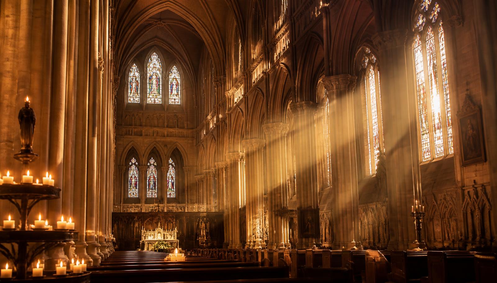 Nef de cathédrale traversée par des rayons de lumière dorée à travers les vitraux